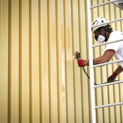 Pracownik w trakcie malowania elewacji blaszanej z blachy trapezowej