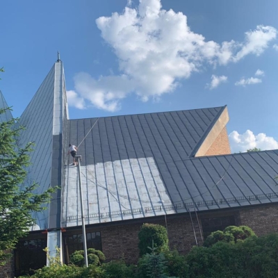 Pracownik w trakcie malowania dachu kościoła