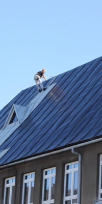 Pracownik w trakcie malowania dachu szkoły