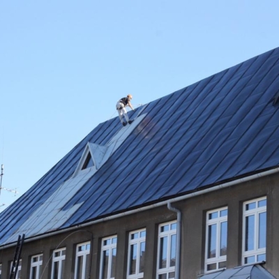 Pracownik w trakcie malowania dachu szkoły
